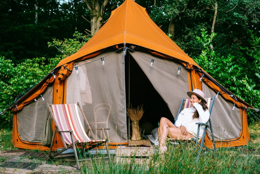 Autentic | Luxury Glamping Bell Tents - Woman sitting in a chair in front of an orange Autentic 5m glamping bell tent which is set up for backyard glamping