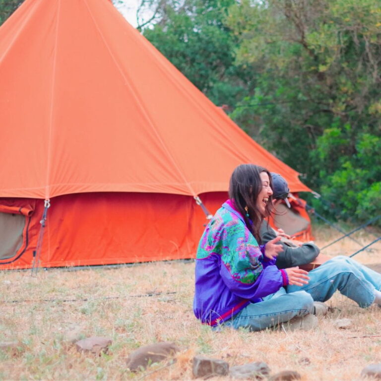 Autentic | Luxury Glamping Bell Tents - A couple laughing in front of a Red Sand Autentic Bell tent at Glamping Revolution